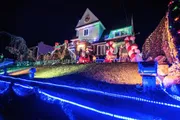 A house is vibrantly decorated with colorful Christmas lights and festive inflatable decorations, including Santa Claus and candy canes, creating a cheerful nighttime holiday scene.