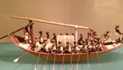 The image shows a detailed model of an ancient Egyptian funerary boat with figures rowing and performing various tasks.