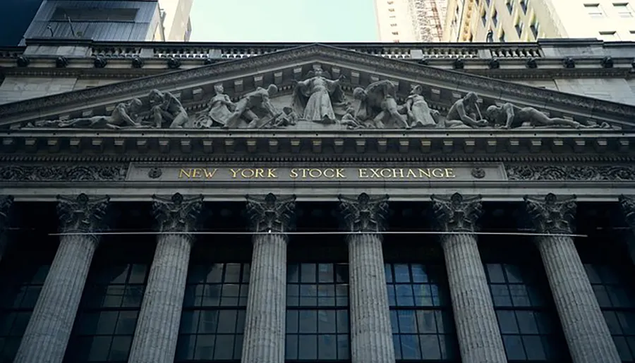 The image showcases the neoclassical facade of the New York Stock Exchange with its columns and distinguished sculpture above the entrance.