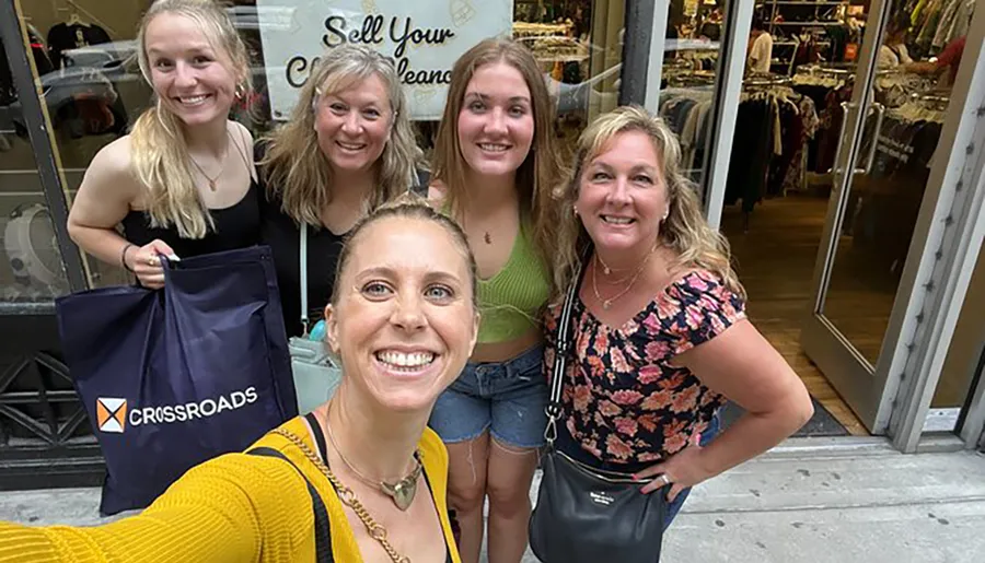A group of five smiling women takes a selfie in front of a clothing store.
