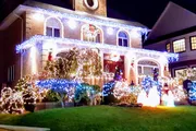 The image shows a two-story house elaborately decorated with festive lights and Christmas decorations, including illuminated figures on the lawn.