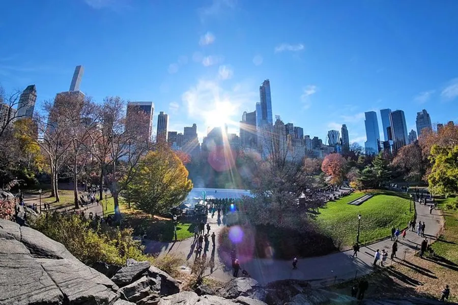 The image depicts a vibrant and sunny day in Central Park with visitors enjoying the natural scenery, framed by the towering skyscrapers of Manhattan in the background.