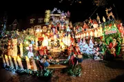 The image shows a house extravagantly decorated with a variety of illuminated Christmas decorations, including Santa Claus figures, reindeer, lights, and festive ornaments.