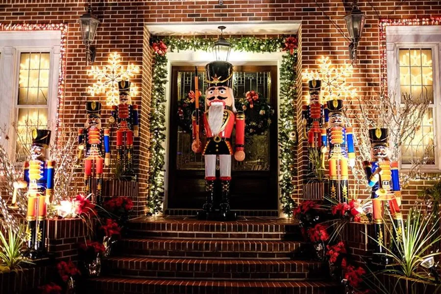 The image shows a festive holiday display at a residential entrance, featuring a large nutcracker decoration flanked by smaller nutcrackers, wreaths, and twinkling lights on a brick facade.