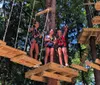 Three individuals are harnessed and smiling on an outdoor high ropes adventure course among the trees