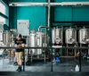 A person is working among several stainless steel brewing tanks in a modern craft brewery