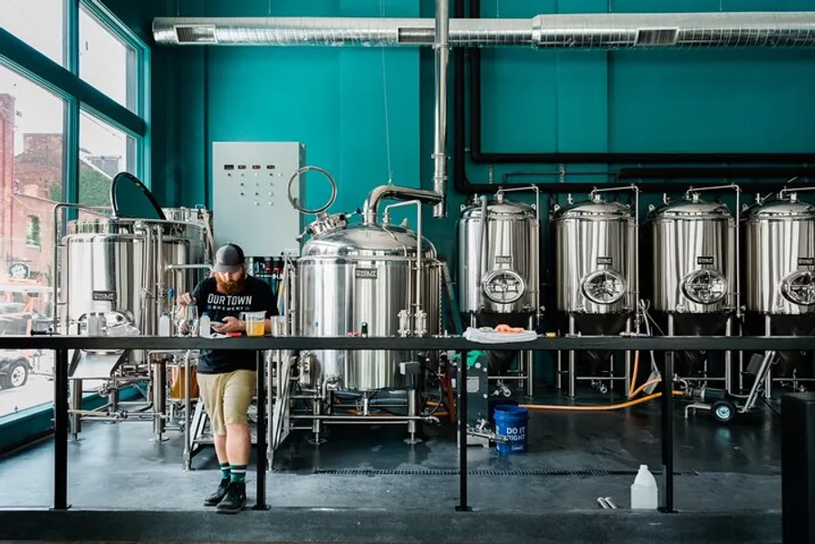 A person is working among several stainless steel brewing tanks in a modern craft brewery.
