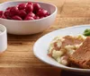 The image shows a plate with traditional German foods including sauerkraut a meatloaf slice with a chili on top a schnitzel and mashed potatoes with gravy accompanied by two side dishes of apple sauce and whipped cream