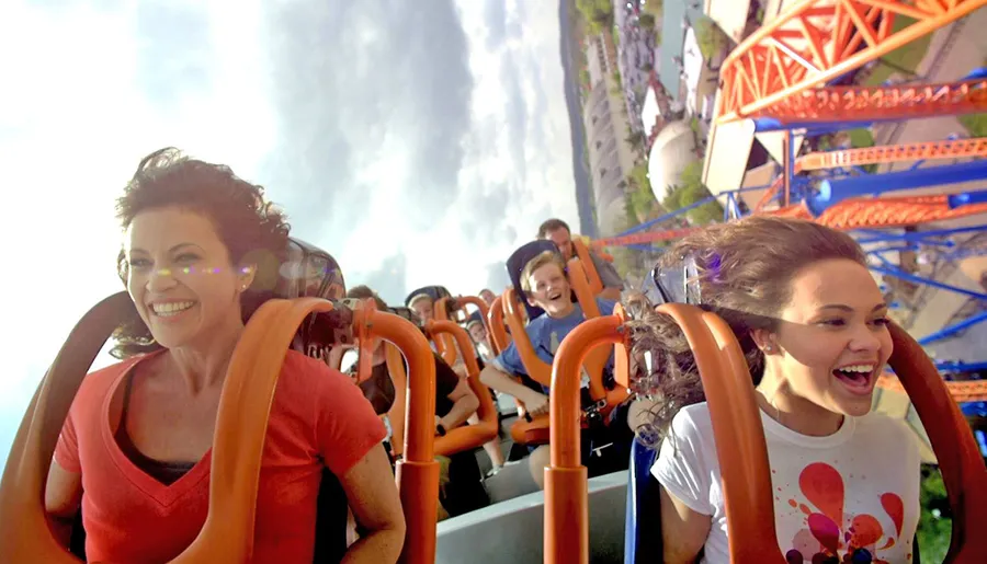 Thrilled riders express joy and excitement on a roller coaster as they descend a steep track under a sunny sky.