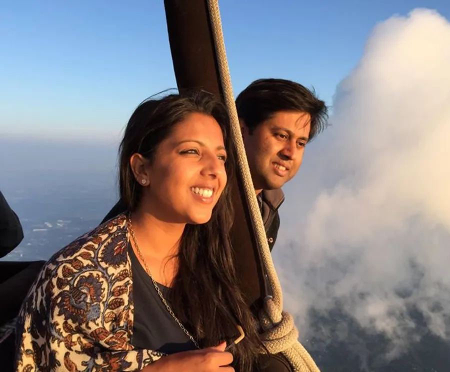 A woman and a man are enjoying a scenic hot air balloon ride high above the clouds during sunset or sunrise.