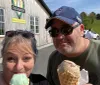 Two people are taking a selfie outside a creamery each holding an ice cream cone and smiling on a sunny day