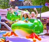 Children are joyfully riding on a colorful frog-themed amusement park ride on a sunny day
