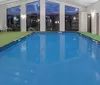 An indoor swimming pool is showcased in a brightly lit room with large windows lounge chairs and a green carpet area reflecting a serene ambiance