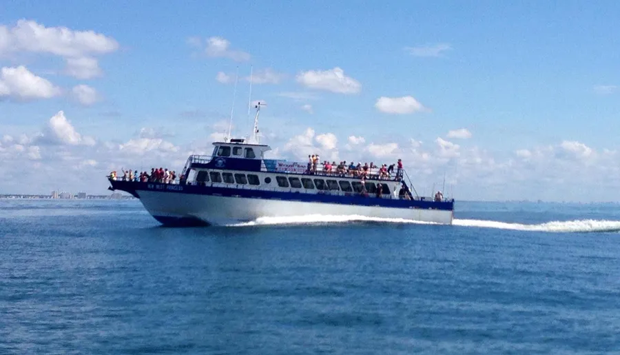 A passenger boat is cruising on the sea under a blue sky dotted with clouds, carrying several people on its decks.