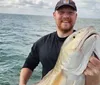 A man is smiling and holding up a large fish he caught while on a boat in the sea