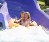 A person is joyfully sliding down a water slide on a yellow inflatable ring