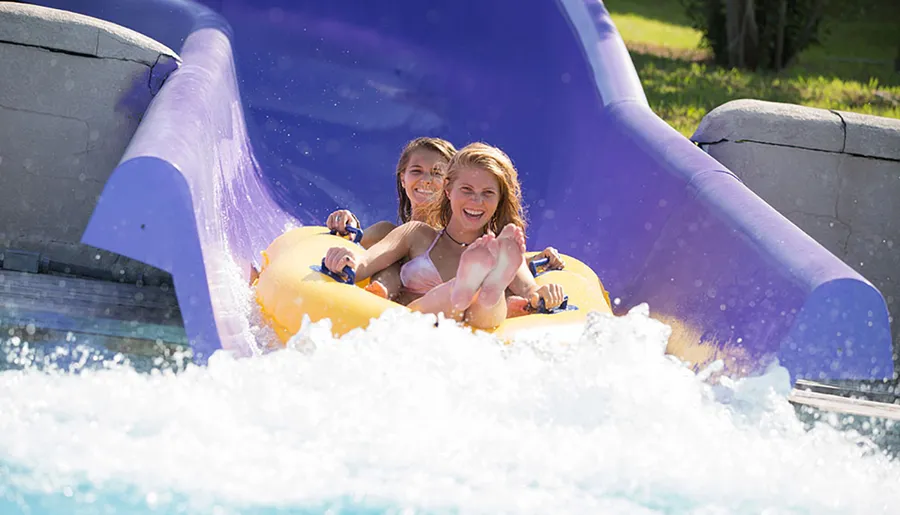 Two people are enjoying a ride down a water slide on a yellow double tube.