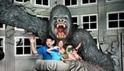A family poses for a playful photo with a large 3D King Kong exhibit as though they are being attacked.