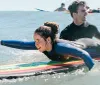 Two people are wearing wetsuits and lying on surfboards paddling in the ocean