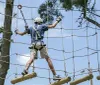 Two people are navigating an outdoor high ropes course among the trees equipped with safety harnesses and helmets
