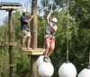 Two people are navigating an outdoor high ropes course among the trees equipped with safety harnesses and helmets