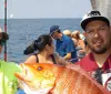 A man is holding a large colorful fish aboard a boat with other people around possibly after a successful fishing trip
