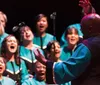 A choir passionately sings on stage as a conductor with their back to the camera leads them with expressive hand gestures