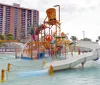 A colorful water playground with slides and splash features in front of a hotel complex