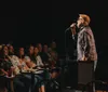 A person is performing stand-up comedy at the Carolina Comedy Club as indicated by the prominent backdrop