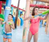 Two children are joyfully playing with water blasters at a colorful splash park