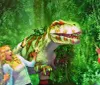 Three people appear to be playfully interacting with a Tyrannosaurus rex in a staged jungle setting