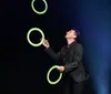 A performer is juggling glowing rings on a stage with a backdrop of bright lights