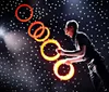 A performer is juggling glowing rings on a stage with a backdrop of bright lights