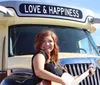 A smiling person is seated in front of a large vehicle with the words LOVE  HAPPINESS displayed on its signboard