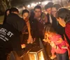 A group of people gathers attentively around a lantern held by a guide during what appears to be a ghost tour at night
