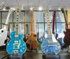The image shows a collection of various electric guitars on display featuring different colors and designs with a reflective floor and large windows in the background of a music store