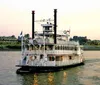 A traditional paddlewheel riverboat is cruising on a river at dusk