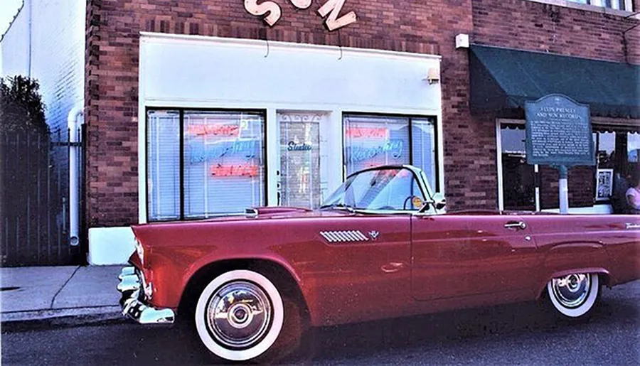 A vintage red car is parked in front of the Sun Studio building, which has a historical marker sign next to it.