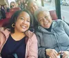 Two smiling women are posing for a photo while sitting on a bus with other passengers in the background