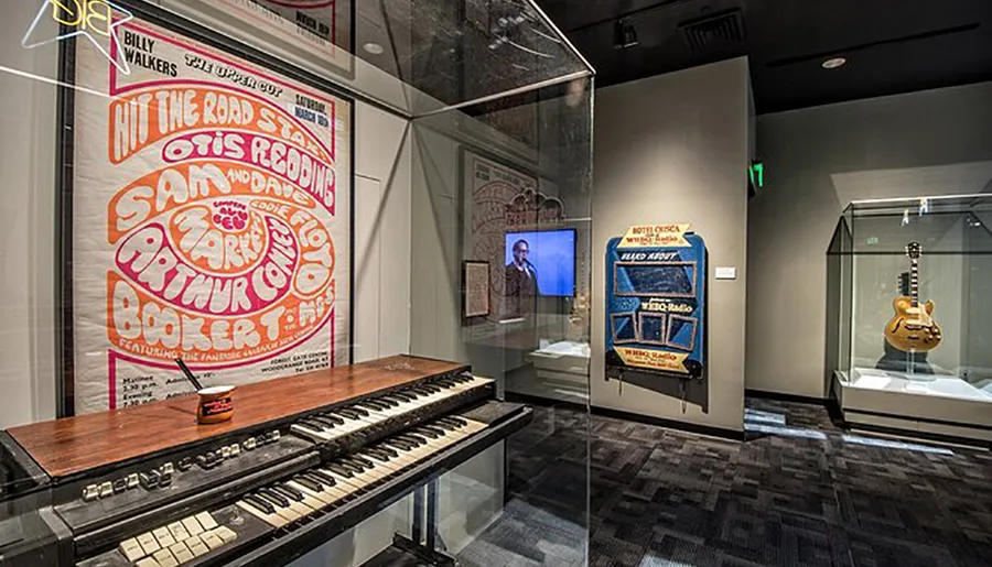 The image shows an exhibit likely within a music museum, featuring a vintage concert poster, an organ keyboard, and other music-related memorabilia.
