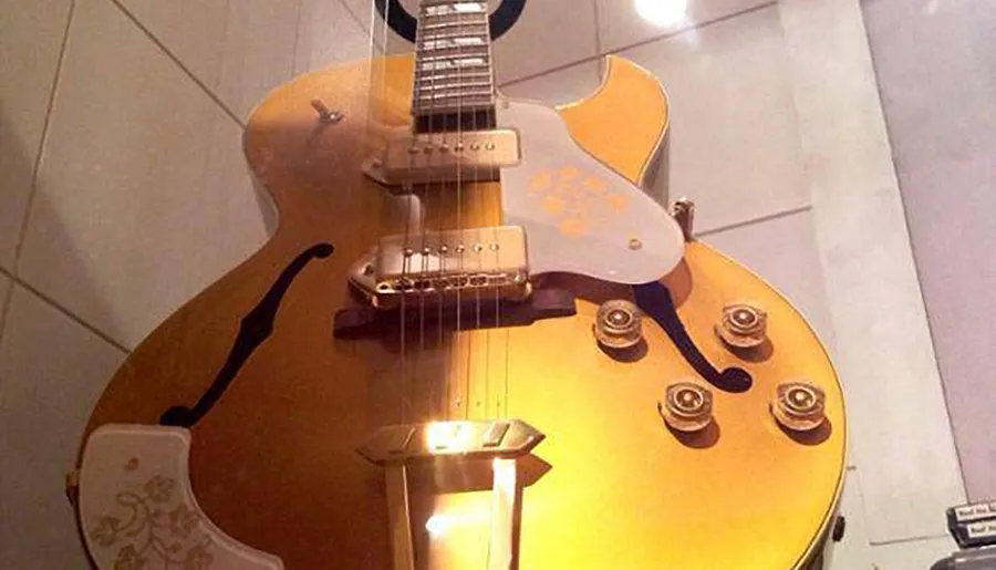 The image shows a close-up of a sunburst electric guitar with a Bigsby-style vibrato tailpiece and two humbucker pickups.