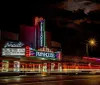 A brightly lit vintage theater marquee stands out against the night sky with streaks of light from passing vehicles blurring in the foreground