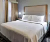This is a neatly presented hotel room with a large bed two bedside tables with lamps and a drawn curtain in the background