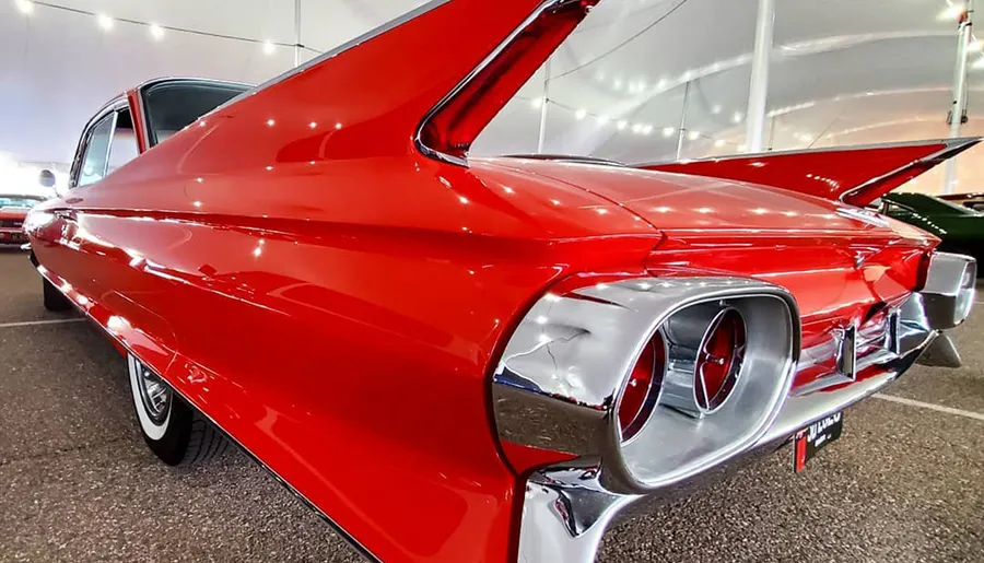 A gleaming red vintage car with distinctive large tail fins and circular taillights is showcased in a covered exhibit space.
