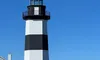 A black and white striped lighthouse stands near a waterfront under a clear blue sky.
