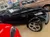 A black convertible car with a unique design is displayed in a showroom alongside other vintage vehicles.