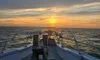 A boat is heading towards a serene ocean sunset beneath a partly cloudy sky.