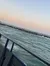 A boat travels near rocky outcrops in a calm sea under a pastel-colored sky.
