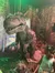 A child is standing in front of a life-sized model of a Tyrannosaurus rex set against a jungle backdrop.
