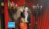 A child stands next to a Dracula wax figure in a staged, gothic-themed area adorned with red curtains and candles, presumably in a wax museum.